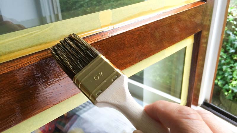 kwast brengt donkerbruine beits aan op kozijn